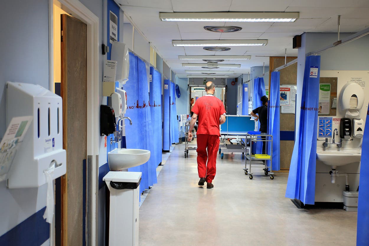 A clinician in scrubs walking down a hospital ward corridor