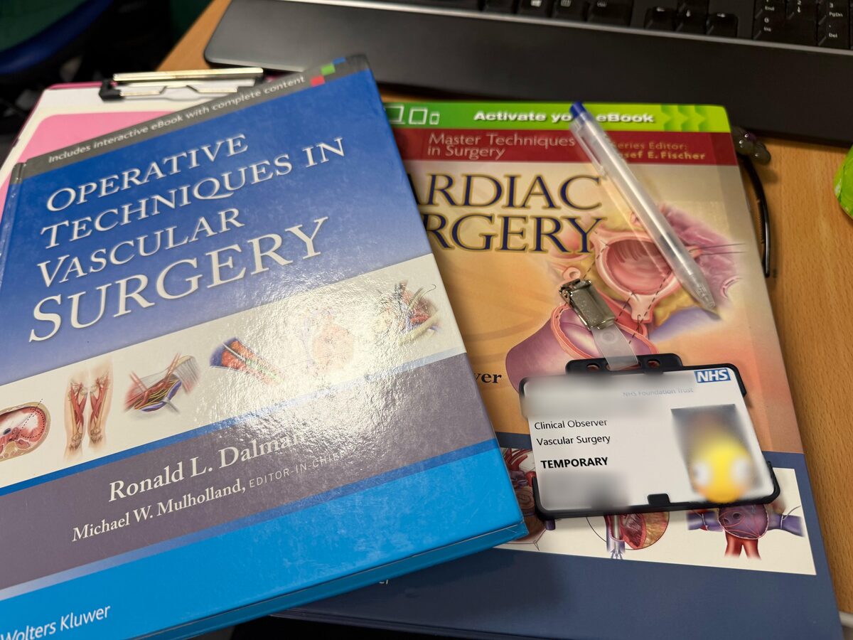 A temporary NHS clinical observer badge for vascular surgery, resting on operative vascular and cardiac surgery textbooks